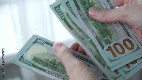 Hands of a woman counting one-hundred dollar bills to pay for expenses, symbolizing the high cost of living, rising inflation, and payment for expensive household utility bills
