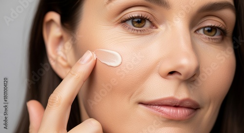 Close up beauty portrait of a mature woman 40 years old is applying a facial skin care cream swatch on her face. 