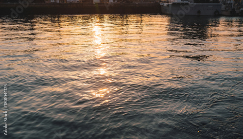 Water surface with sunlight reflections and distant harbor structures.