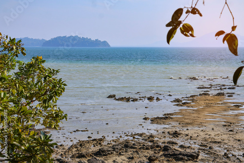 Exposed rocky tropical beach during low tide with an isolated mountainous island.