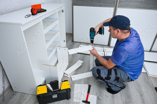 Man using power tool for home improvement, assembling white cabinet in his room
