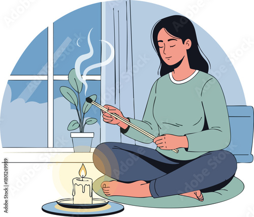 Woman sits cross-legged on a mat, holding incense stick near a lit candle and plant on a windowsill with aids for relaxation.