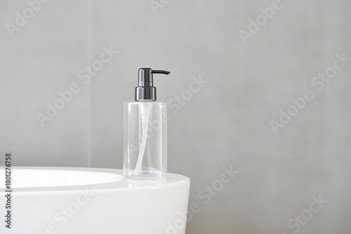 Clear soap dispenser with black pump on a white surface against a gray wall