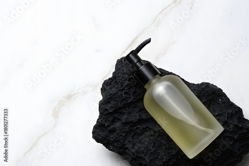 Minimalist skincare bottle on dark textured rock against white marble