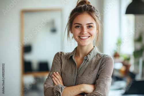 Confident young woman in beige shirt with friendly smile in office. Casual professional image for business communications and corporate content. Copy space