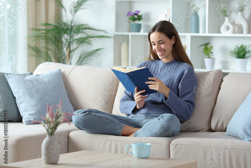 Happy woman in blue reading a paper book at home