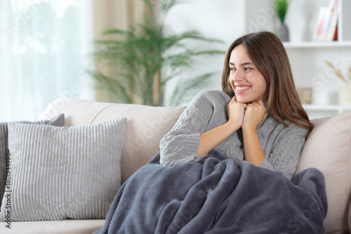Happy woman in grey keeping warm with sweater and blanket