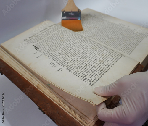 Tableau sur toile Close-up of gloved hands cleaning the pages of an old book with a flat brush