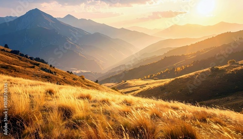 A majestic mountain range is bathed in the warm glow of golden hour sunlight, with dry, golden grass covering the foreground hills.