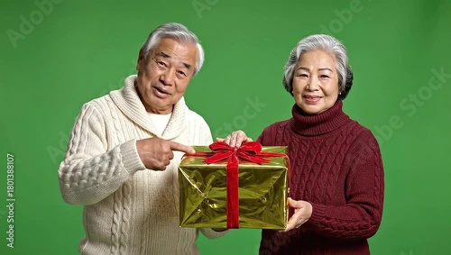 Elderly Asian couple exchanging a golden gift box with a red ribbon on a green screen.