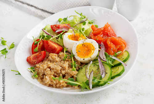 Breakfast oatmeal porridge with boiled eggs, salt salmon, tomatoes, cucumber and red onions. Healthy balanced food.