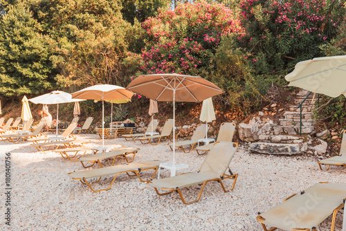 Fototapeta Naklejka Na Ścianę i Meble -  Sunlit lounge chairs and umbrellas on rocky beach retreat
