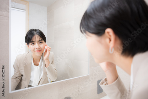 鏡の前で笑顔で身だしなみを整える女性の美容、メイク直しなどのシーン　