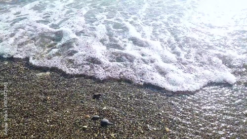 The sea, sand, waves, and foam fill part of the pebble shore. Background.