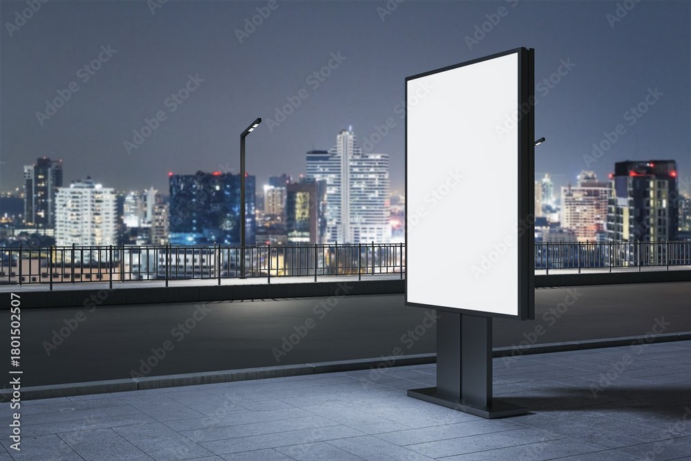 Obraz premium Vertical blank billboard mockup on city street at night with urban skyline and lights in background for advertising and branding presentation. 3D Rendering