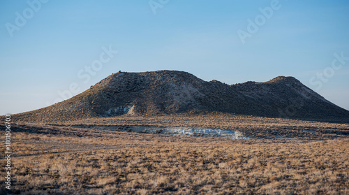 barren landscape with dry grass and rocky hills under clear blue sky, rugged terrain with visible erosion and sparse vegetation, remote and arid environment, vast natural scenery
