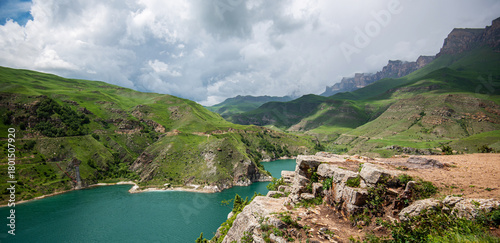 Turquoise lake nestled in green mountainous terrain, under a dramatic cloudy sky, showcasing nature's contrast between water and land