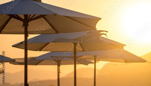 Beach umbrellas glow in the warm, golden light of sunset, creating a serene vacation vibe