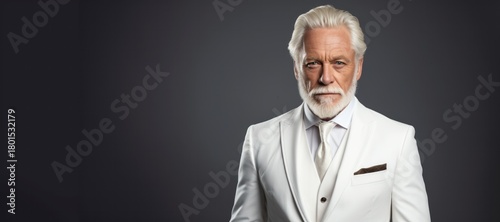 Mature man with silver hair and beard, dressed in a stylish white suit, poses confidently against a dark background, exuding elegance and sophistication in a portrait setting