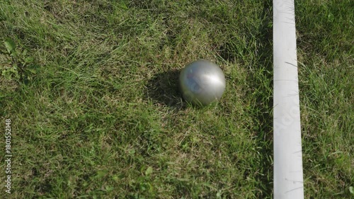A metal throwing ball falls on the lawn next to the markings