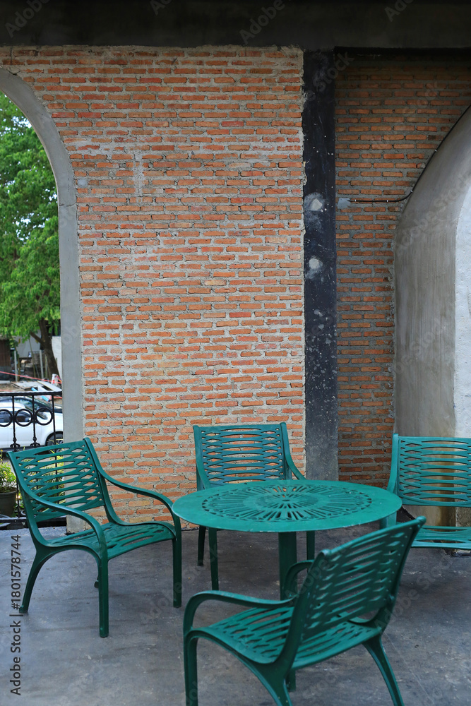 Fototapeta premium A charming outdoor seating area featuring vibrant green metal chairs and a matching round table, set against a rustic exposed brick wall.