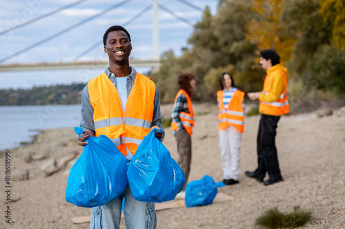 Portrait of smiling male volunteer in a safety vest holding trash bags during a community environmental cleanup event.