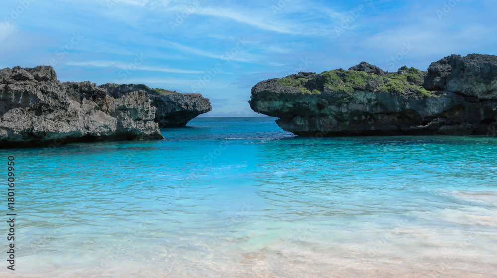 Fototapeta premium A calm turquoise lagoon sits between rugged cliffs under a bright blue sky, creating a peaceful and vibrant tropical scene.