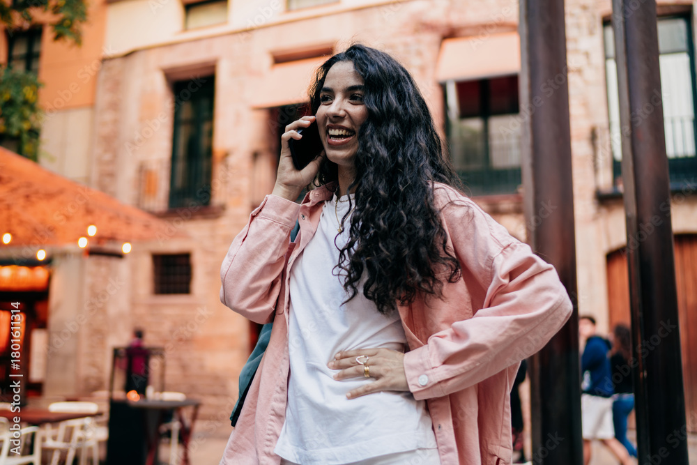 Obraz premium Joyful woman laughs on phone call, one hand on hip, expressing empowerment, real-time digital connection and dynamic self-confidence in freelance lifestyle.