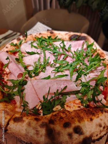 Delicious Italian pizza with mortadella, arugula, pistachiosnd melted cheese on a crispy crust. Gourmet restaurant dish with fresh ingredients and authentic Mediterranean flavor. 