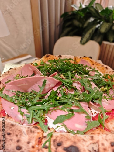 Delicious Italian pizza with mortadella, arugula, pistachios, and melted cheese on a crispy crust. Gourmet restaurant dish with fresh ingresients and authentic Meditarranean flavor