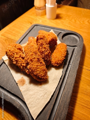 Crispy fried chicken wings in golden breading served on lavash bread over a rustic wooden board. Tasty snack, American and European comfort food close-up.
