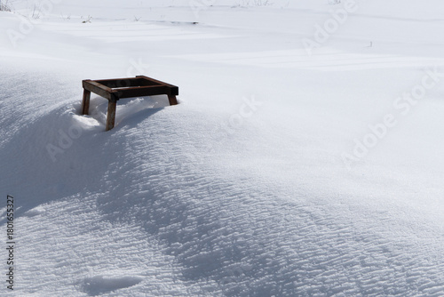 Wooden platform sits atop a snow-covered hill, surrounded by a vast expanse of white snow, reflecting bright sunlight, creating a serene winter landscape with tranquility