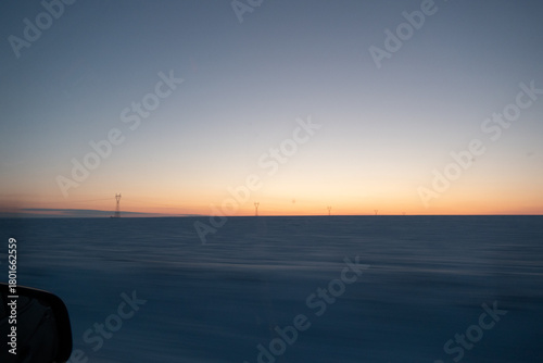 Expansive winter landscape at dusk, showcasing a serene horizon with wind turbines silhouetted against a colorful sky, creating a tranquil and peaceful atmosphere