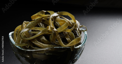 Seaweed salad in a glass bowl on a beautiful black background with light reflections. Healthy food.