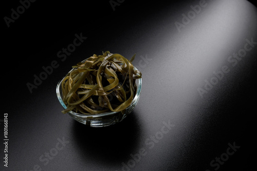 Seaweed salad in a glass bowl on a beautiful black background with light reflections. Healthy food.