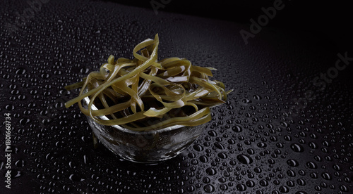 Seaweed salad in a transparent glass cup on a black background with water drops. Healthy food.