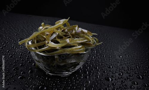 Seaweed salad in a transparent glass cup on a black background with water drops. Healthy food.