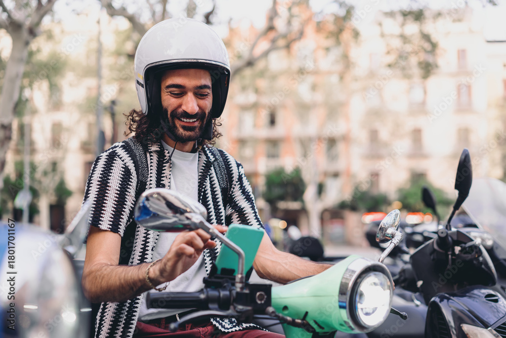 Naklejka premium Smiling man sits on scooter using smartphone, surrounded by bikes, enjoying mobile tools and intuitive navigation in modern connected commuting life.