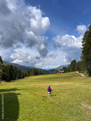 bambino corre in prato tra le montagne con casco da ciclista