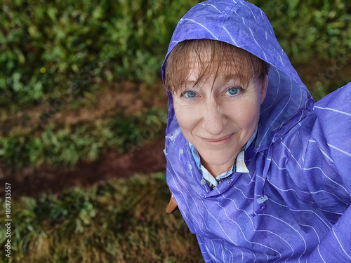 On a rainy day, a seasoned blonde blogger embarks on an adventurous journey through nature, wearing a striking vibrant purple poncho