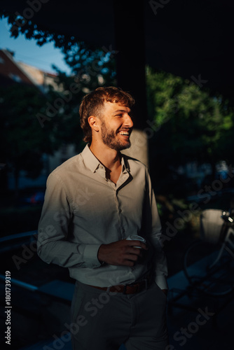 Businessman smiling and holding a coffee cup while standing near some trees