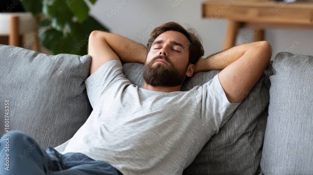 Obraz premium Man relaxing on a couch with hands behind his head in a cozy living room during the day