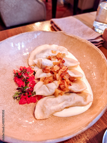 Traditional dumplings served with sour cream, crispy fried onions, and fresh microgreens. Comforting Eastern European dish with rustic presentation and warm, homemade flavors.