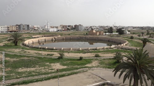 Historic water reservoirs, known as the Aghlabid Basins, with residential neighborhood and mosque in the background, in Kairouan, Tunisia
