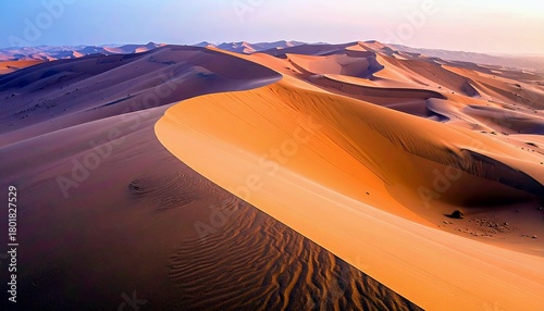 Fototapeta Naklejka Na Ścianę i Meble -  Expansive desert landscape featuring dramatic, sculpted sand dunes with rippling textures, bathed in the warm light of dawn or dusk.