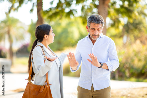 Couple arguing with defensive gestures in a heated outdoor discussion