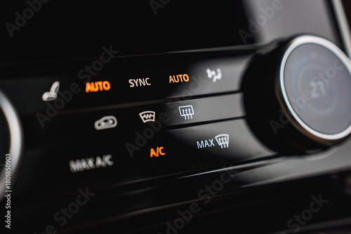Illuminated AUTO, SYNC, A C, MAX defrost, and rear defog icons glow on a glossy panel with a rotary dial near 21 C, shot indoors in a high end workshop with shallow depth of field
