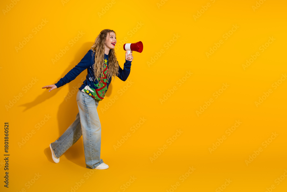 Obraz premium Festive young woman with megaphone in cheerful sweater on yellow background celebrating holiday joy and bright vibes