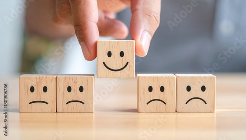 A hand places a smiling block among sad ones, symbolizing positivity and emotion in a creative context.