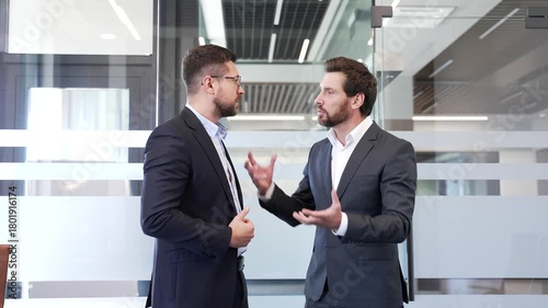 Two angry businessmen arguing intensely in modern office setting, showcasing conflict and emotion during heated business discussion or disagreement. Colleagues aggressive fight, disputing, quarreling